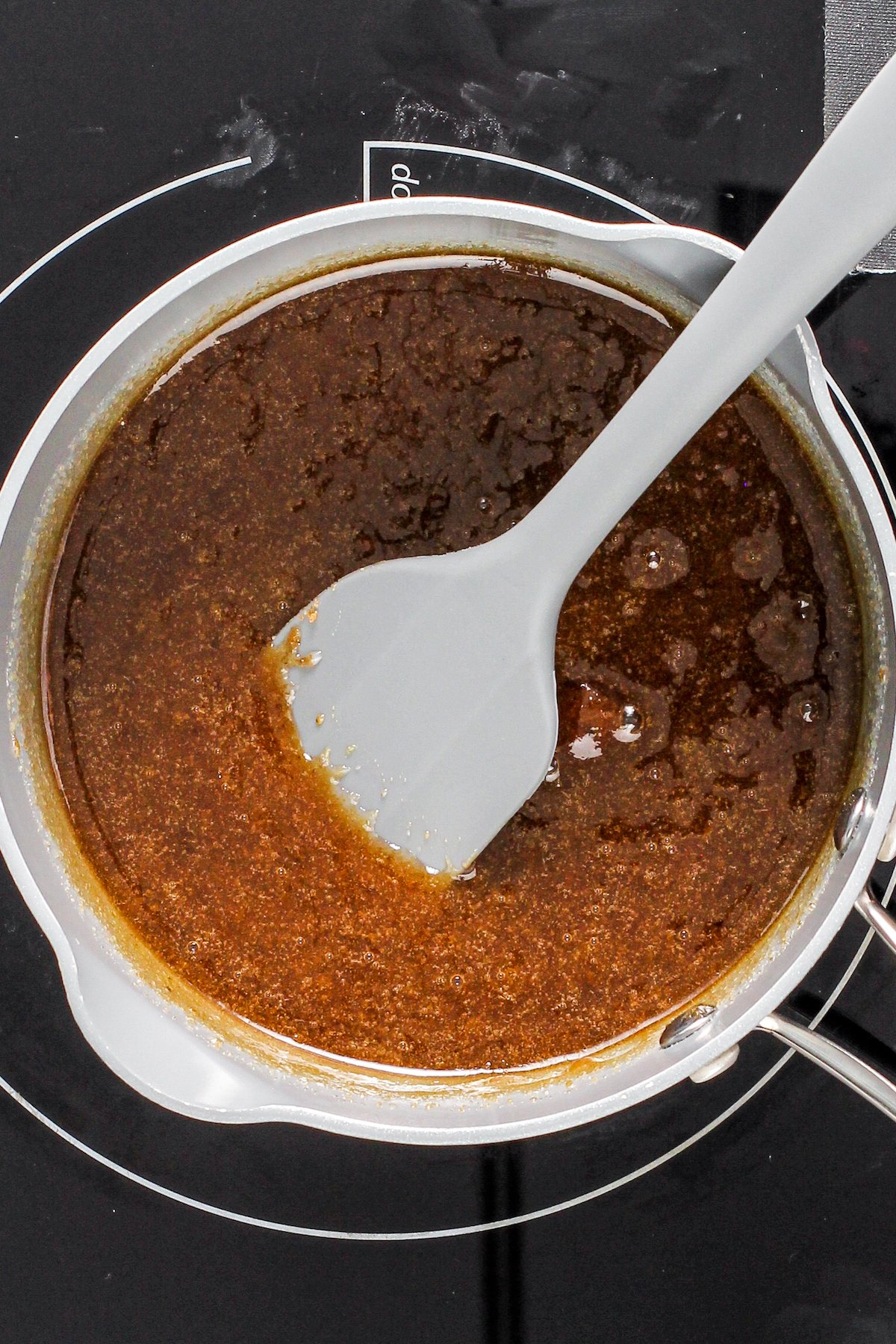 Butter, heavy cream, sugar and more boiling in a sauce pan with a spatula.