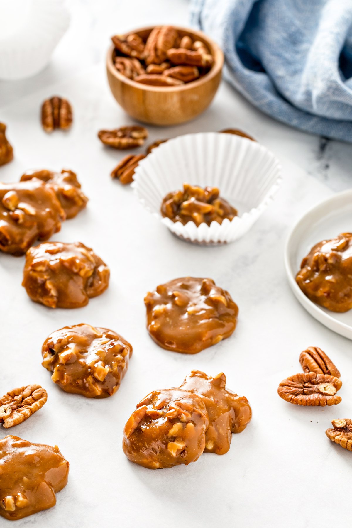 Caramel pecan candies stacked around on parchment paper with a bowl of pecans.