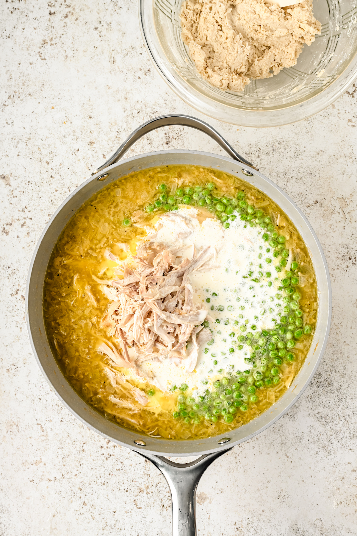 Adding chicken, cream, and peas to a skillet of sauce.