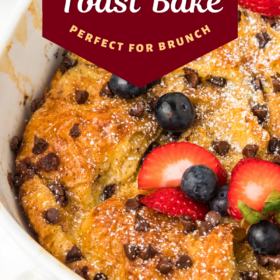 French toast bake with chocolate chips in a casserole dish sprinkled with powdered sugar with fresh fruit on top.