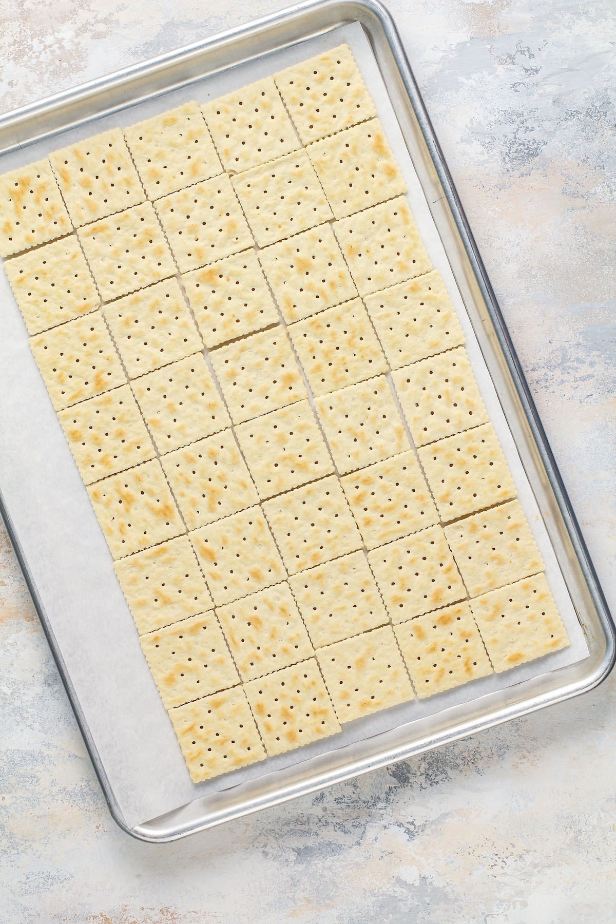 Saltine crackers lined up on a parchment paper lined cookie sheet.