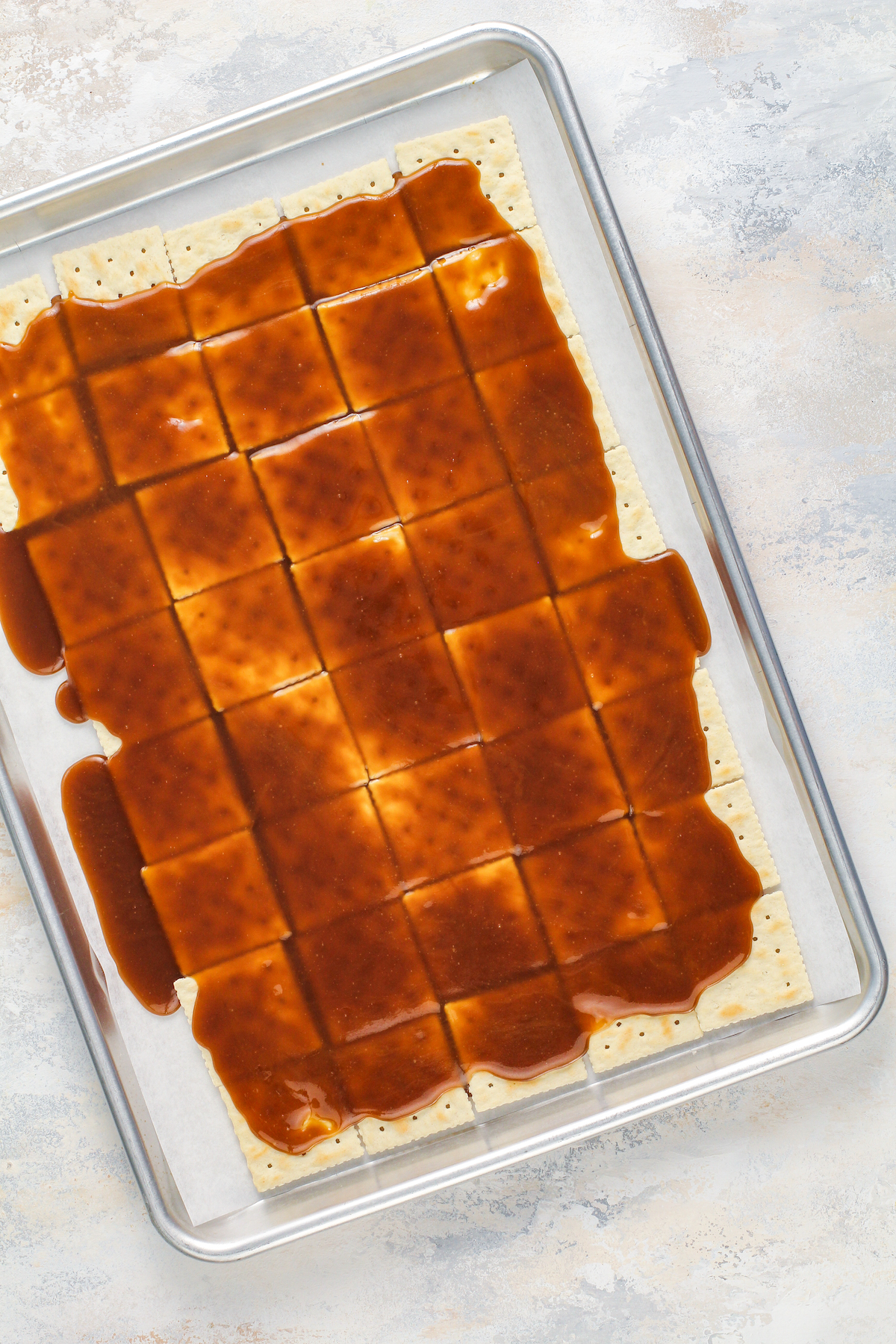Toffee poured on top of lined up saltine crackers on a cookie sheet lined with parchment paper.