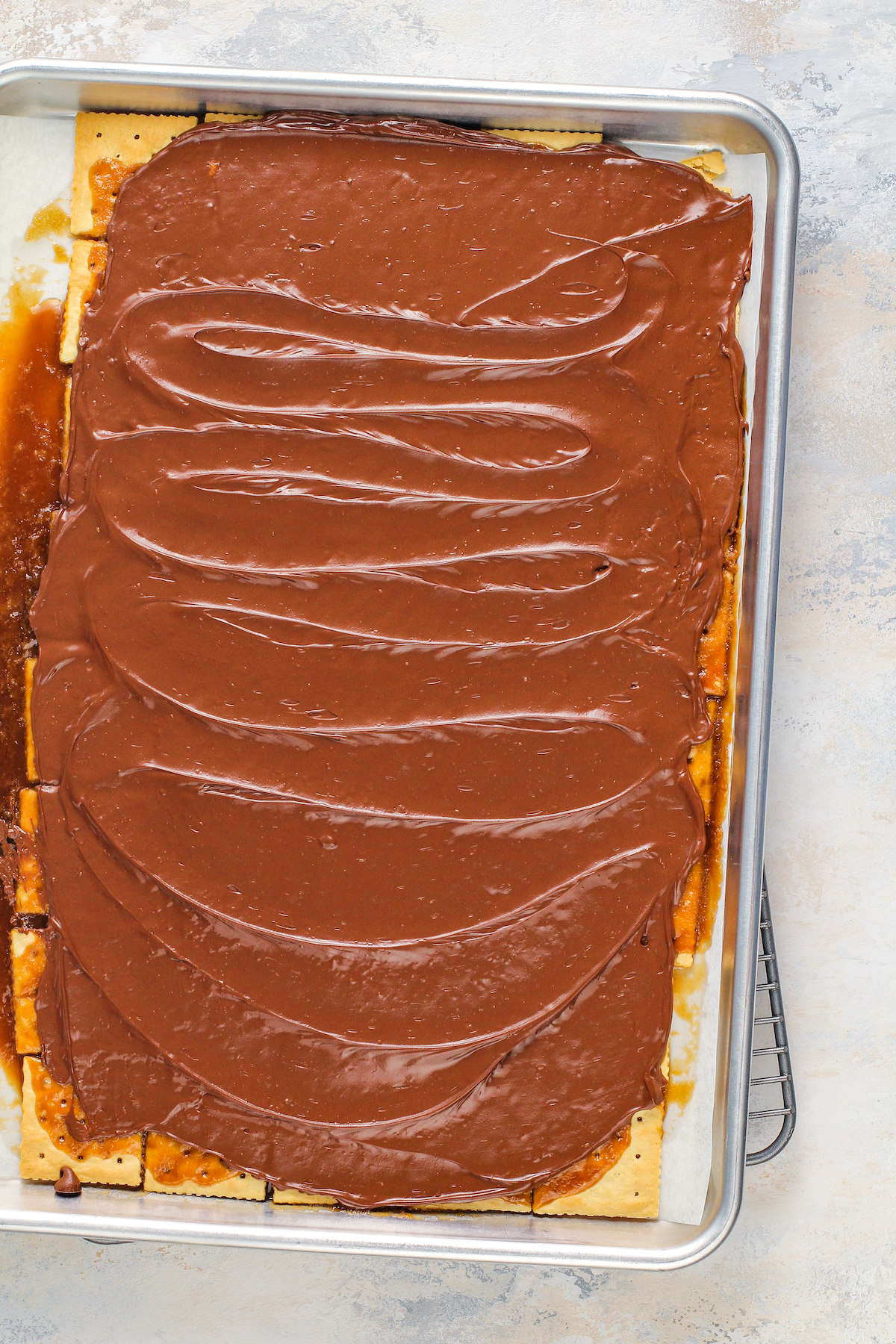 Chocolate spread on top of toffee on top of crackers on a cookie sheet lined with parchment paper.