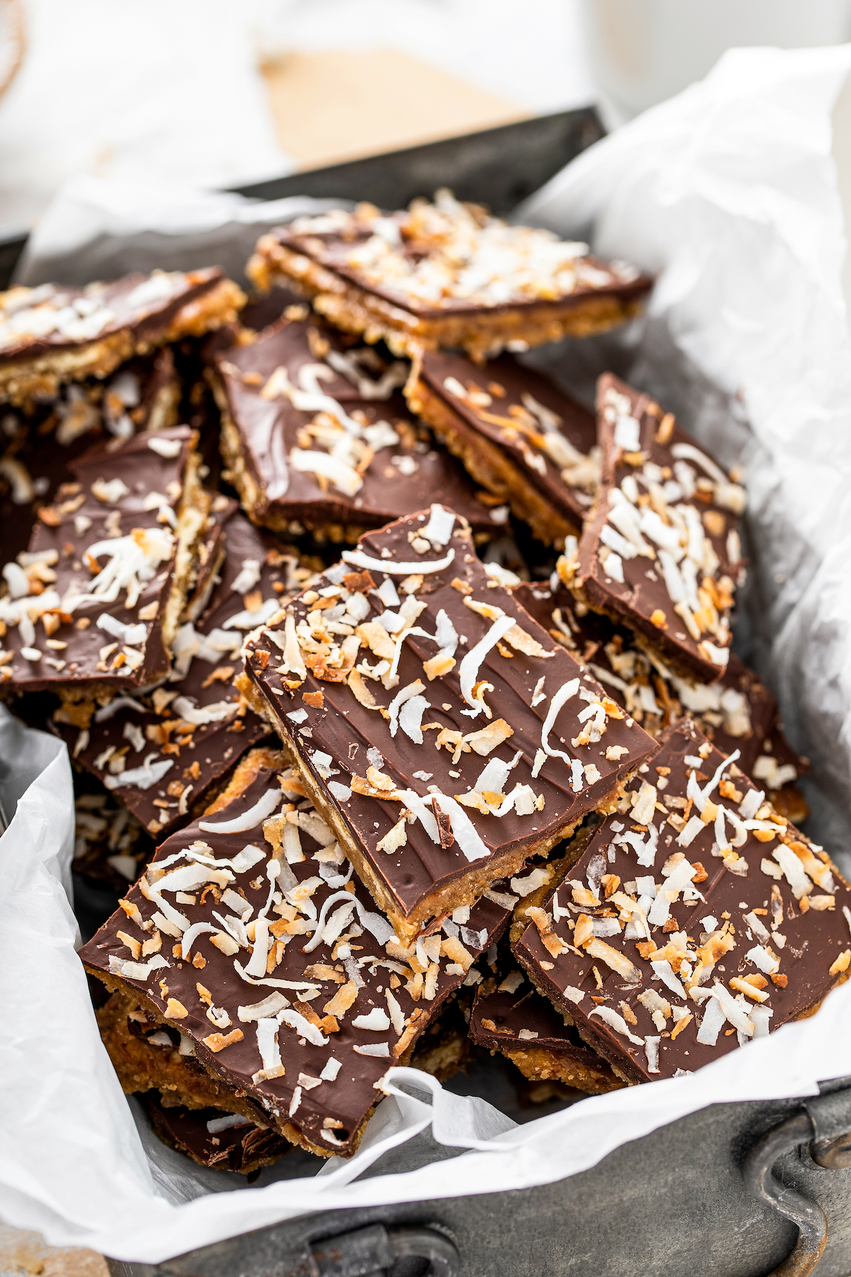 Coconut saltine cracker toffee stacked in a tin lined with parchment paper.