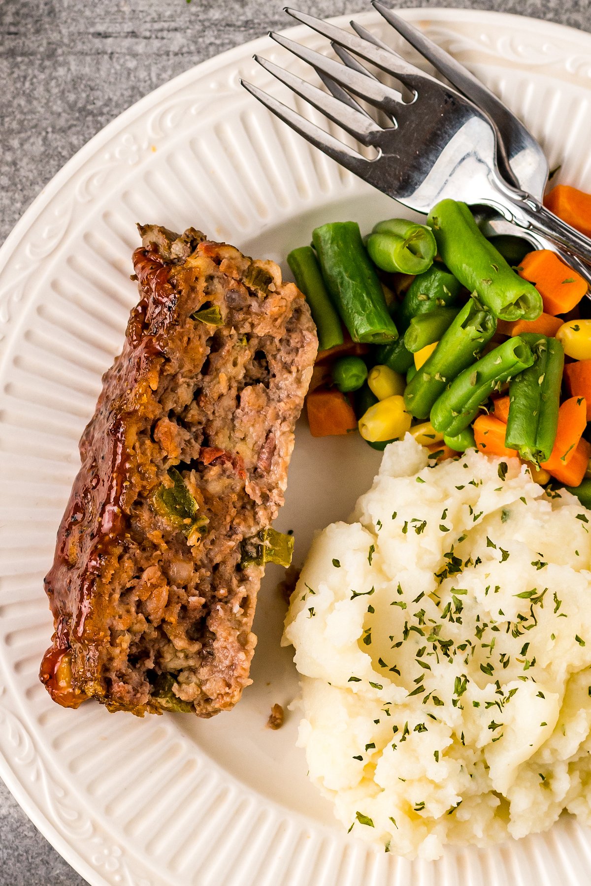 A dinner plate with ground beef loaf, mashed potatoes, and mixed vegetables.