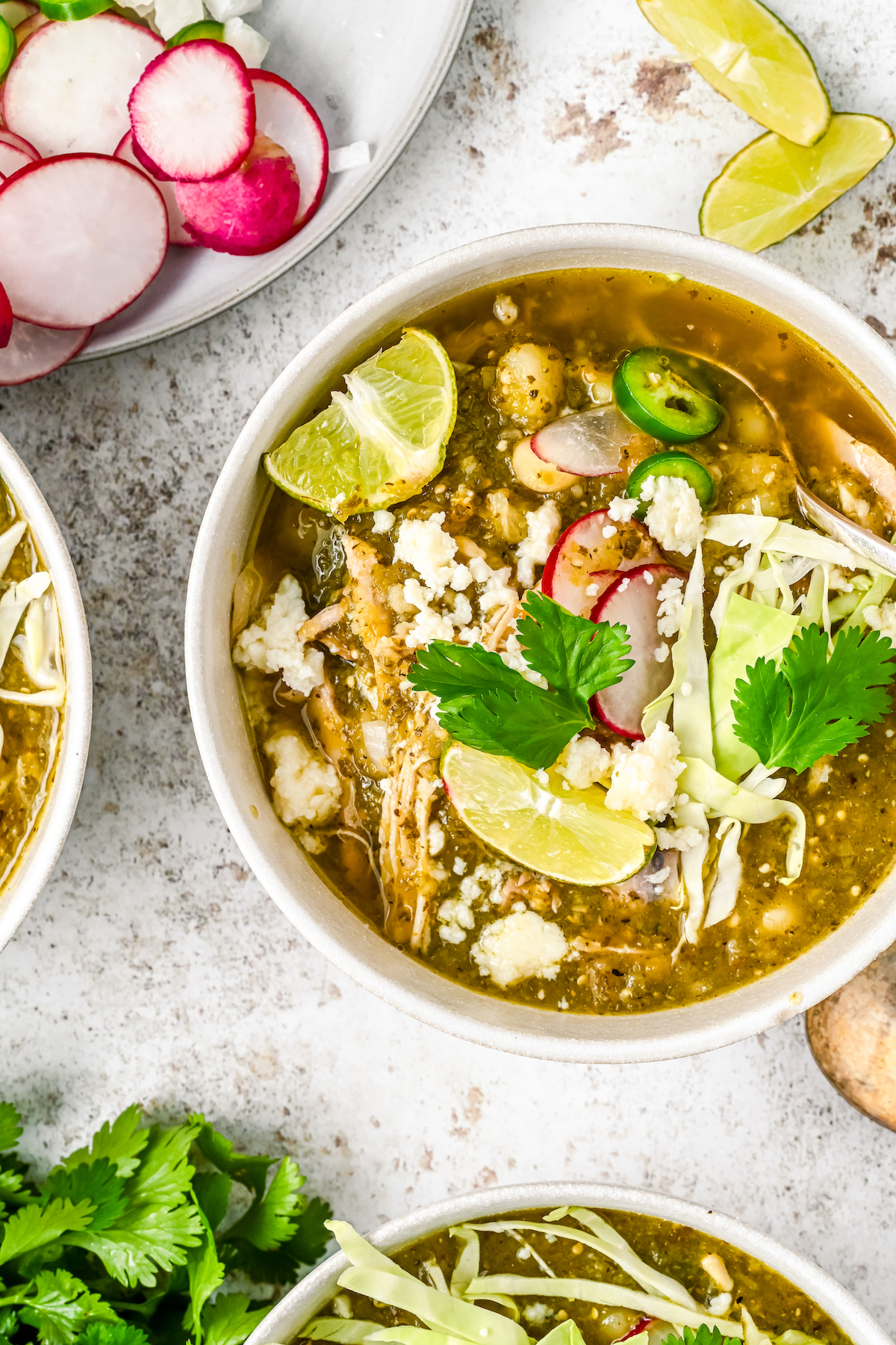 Bowl of Mexican pozole with cilantro, radishes, and a lime wedge.