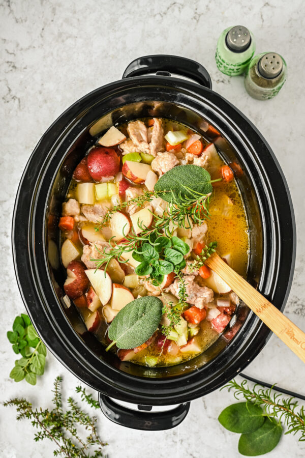 Chicken, vegetables, broth, and herbs in a slow cooker.