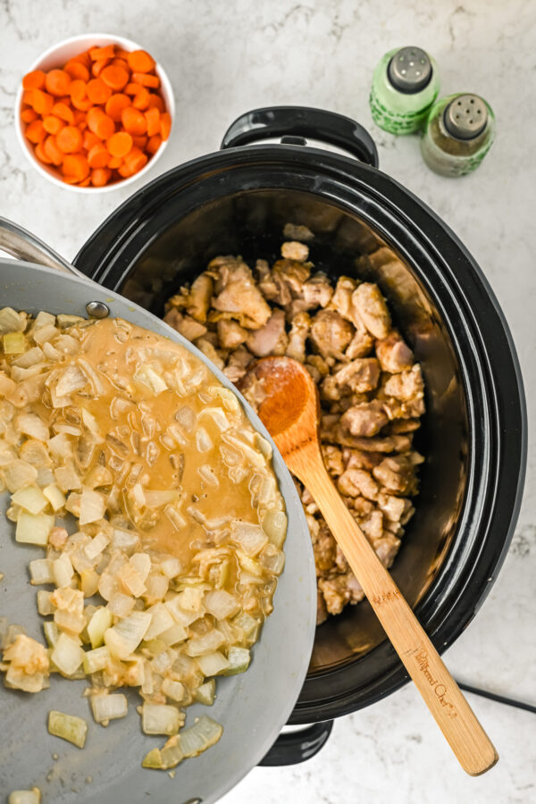 Pouring onions and sauce over chicken in a crock pot.