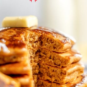 Pancakes stacked on a plate with a bite taken out of them.