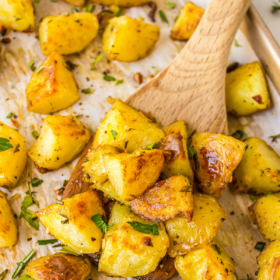 Roasted potatoes on a cookie sheet with a wooden spoon scooping some up.