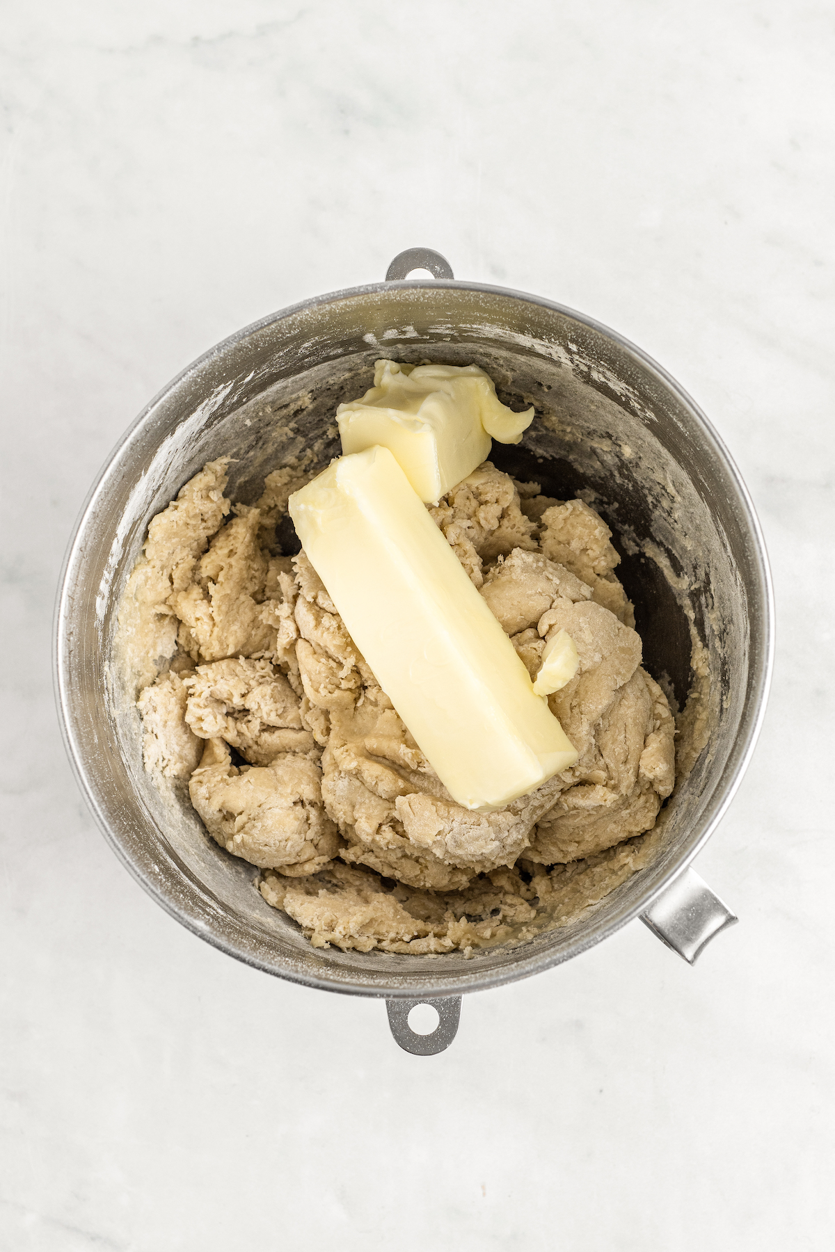 Adding butter to a rough dough in the bowl of a stand mixer.