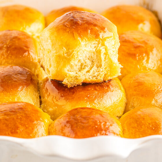 A white baking dish full of dinner rolls. One dinner roll is sitting on top of the rest.