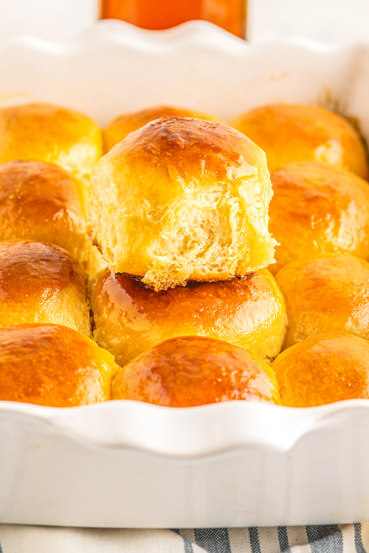 A white baking dish full of Hawaiian dinner rolls. One soft and sweet yeast roll is sitting on top of the rest.