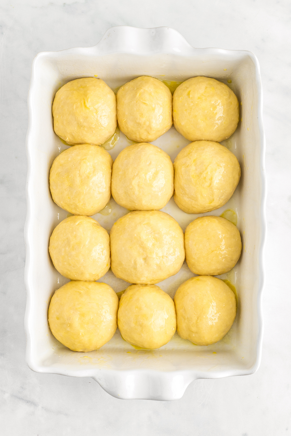 Yeast rolls rising in a large buttered baking dish.