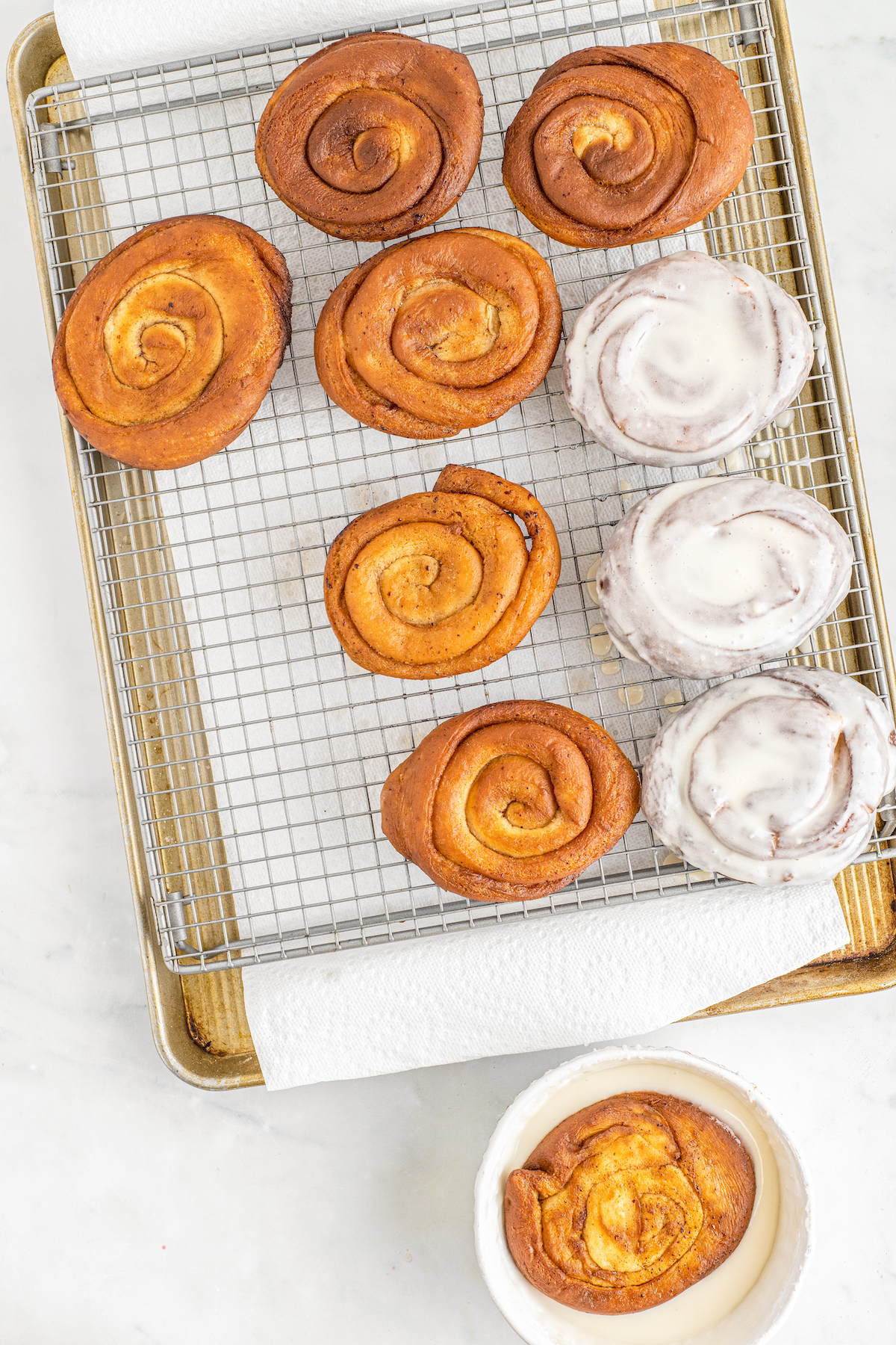 A wire rack over a parchment-lined baking sheet. Honey buns are on the rack, half of them glazed and half of them plain.