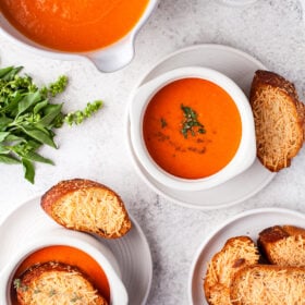 Bowls of tomato soup with cheesy baguette slices.
