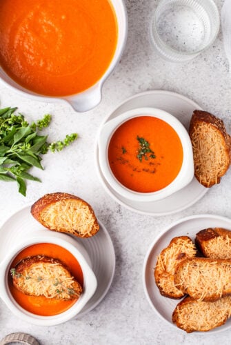 Bowls of tomato soup with cheesy baguette slices.