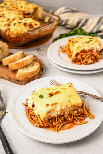 A pasta bake dinner casserole, with servings on a plates nearby. A cutting board with bread is also on the table.