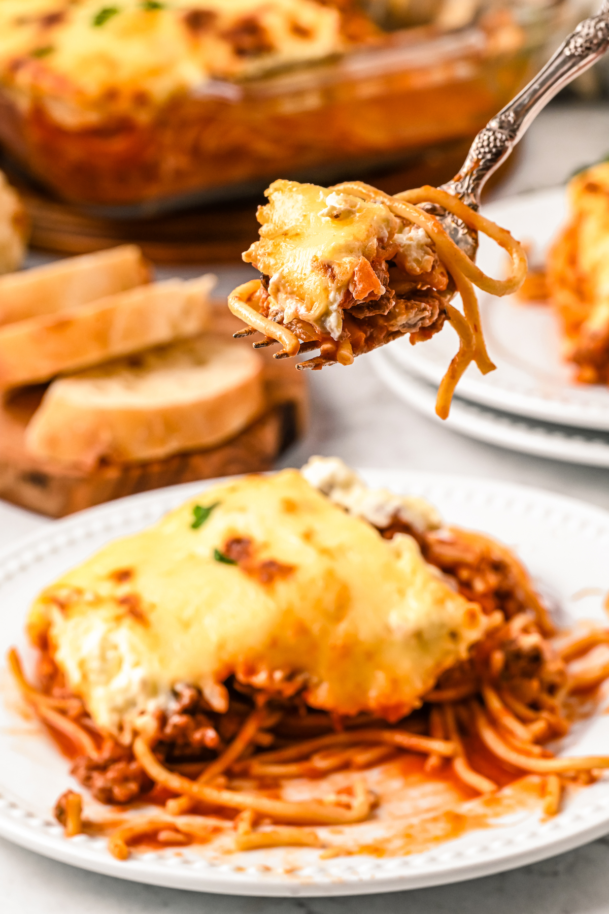 A dinner plate of baked pasta with a fork lifting a bite toward the camera.