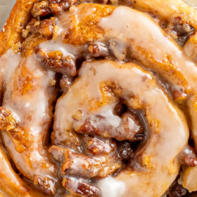 Pecan pie cinnamon rolls on a plate with icing on top.
