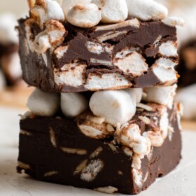 Squares of chocolate fudge with marshmallows and nuts stacked on top of each other.