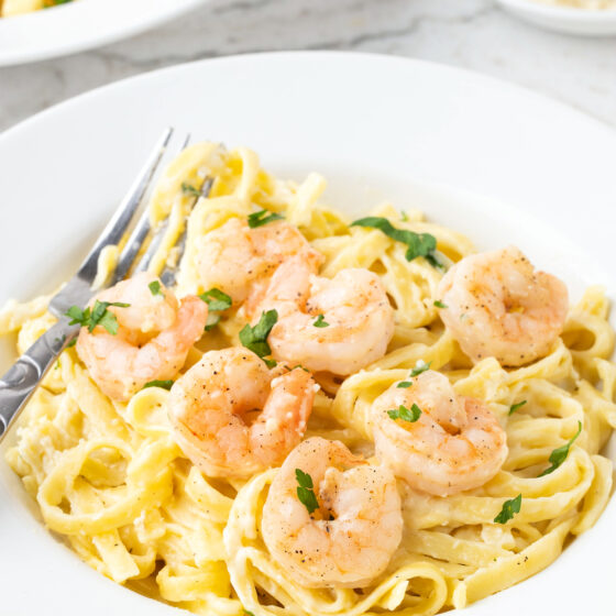 A serving of creamy shrimp alfredo in a large, shallow dinner bowl.