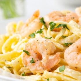 Side view of a plate of shrimp alfredo garnished with parsley.
