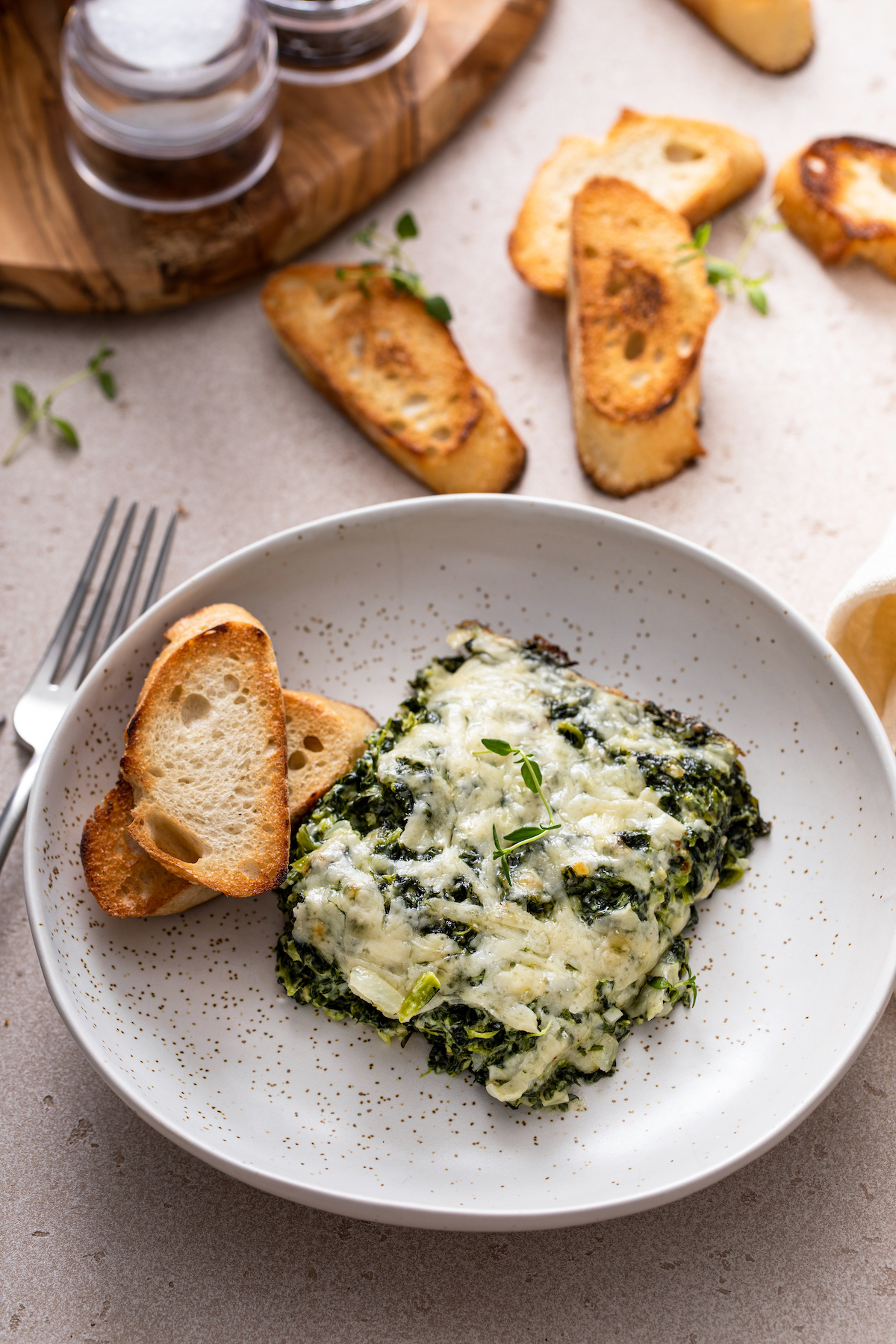 A bowl with a serving of spinach casserole and two toasts.