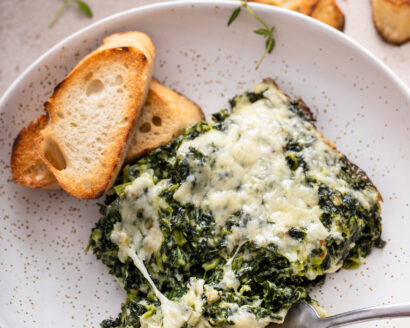 A serving of spinach gratin on a plate with a fork taking a bite.