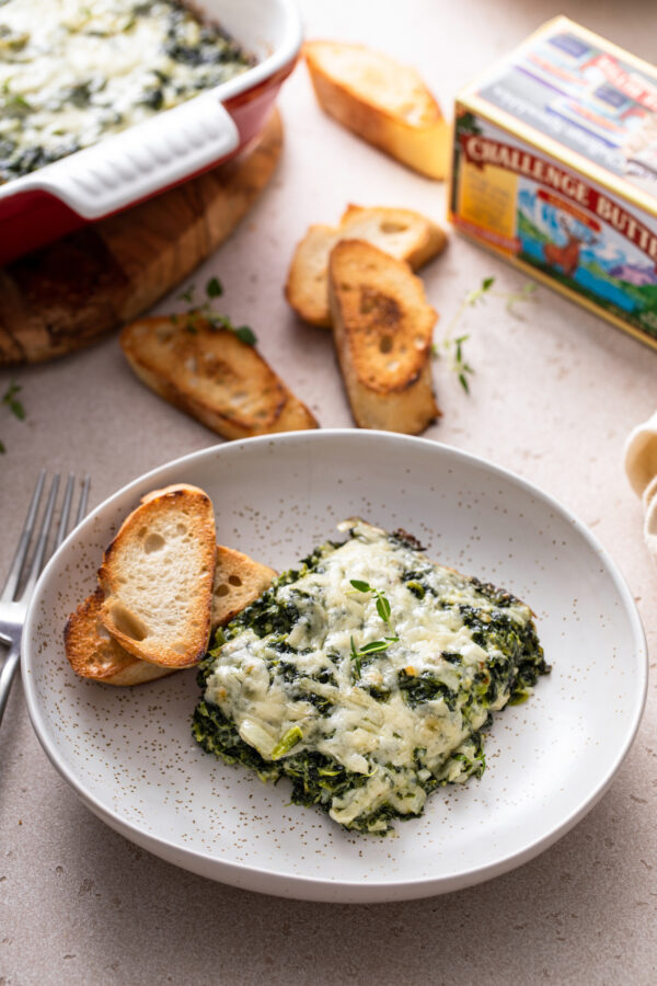 Cheesy spinach casserole on a plate with two toasts and a fork.