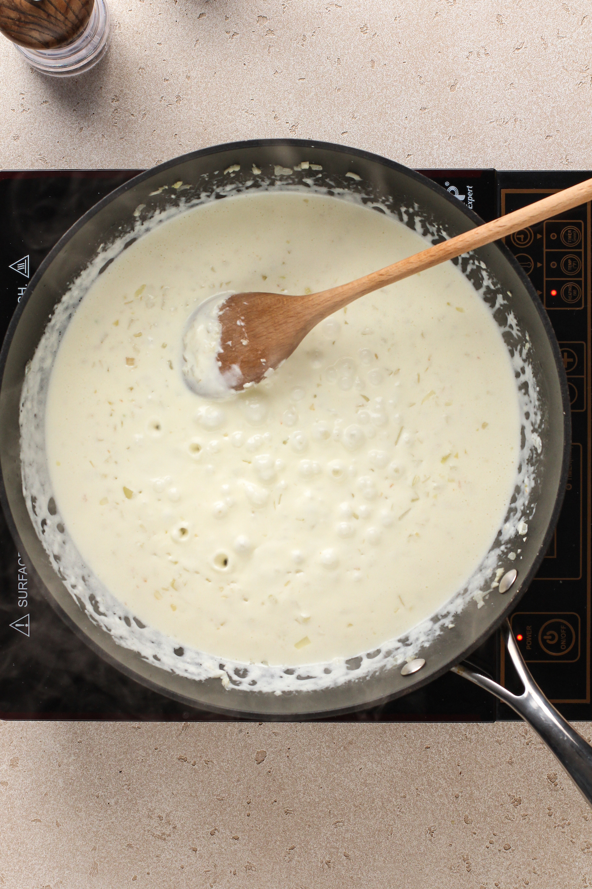 Creamy white sauce in a skillet with a wooden spoon stirring it.