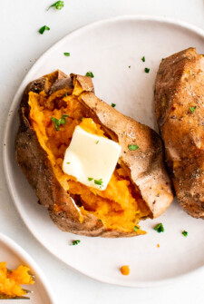 Split and buttered air fryer sweet potatoes on a white plate.