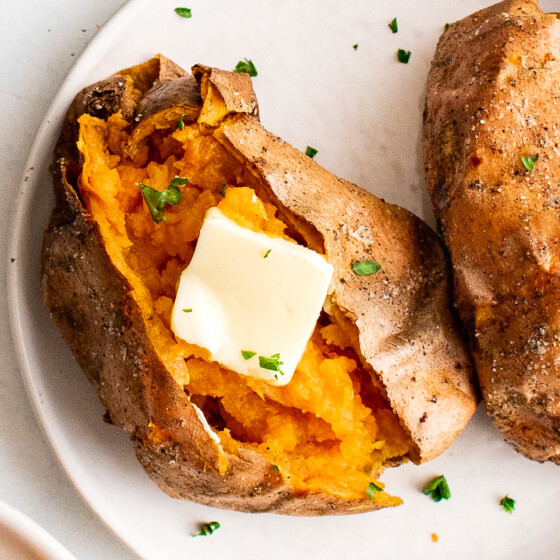 Split and buttered air fryer sweet potatoes on a white plate.