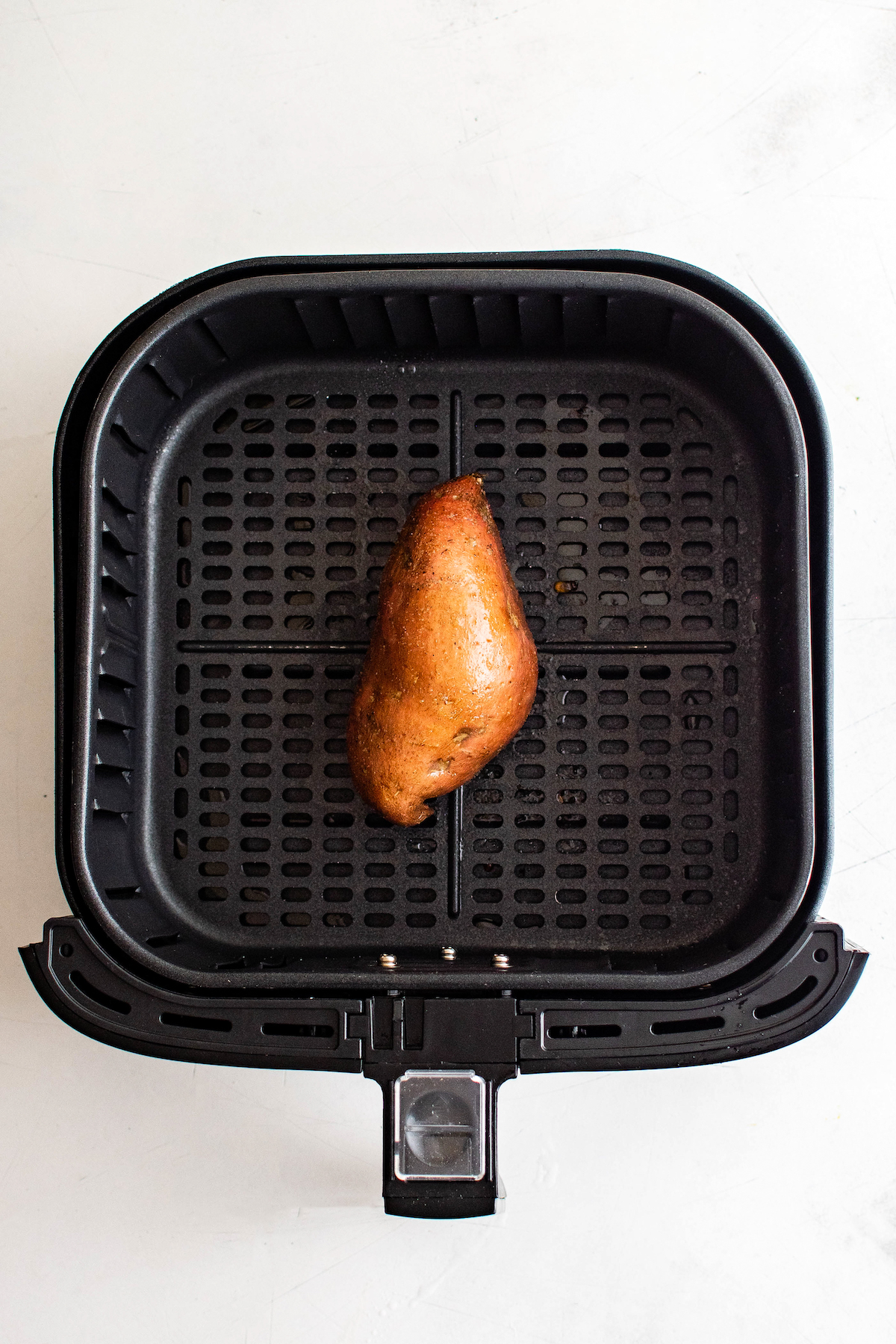 A sweet potato in an air fryer basket.