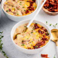 Two bowls of corn chowder with bacon, cheese and chives on top with a spoon.