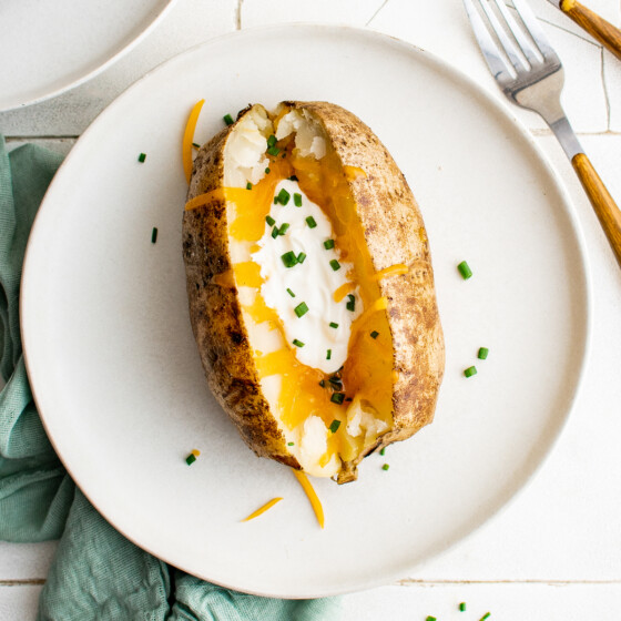 A baked potato on a small plate, topped with sour cream and cheese.