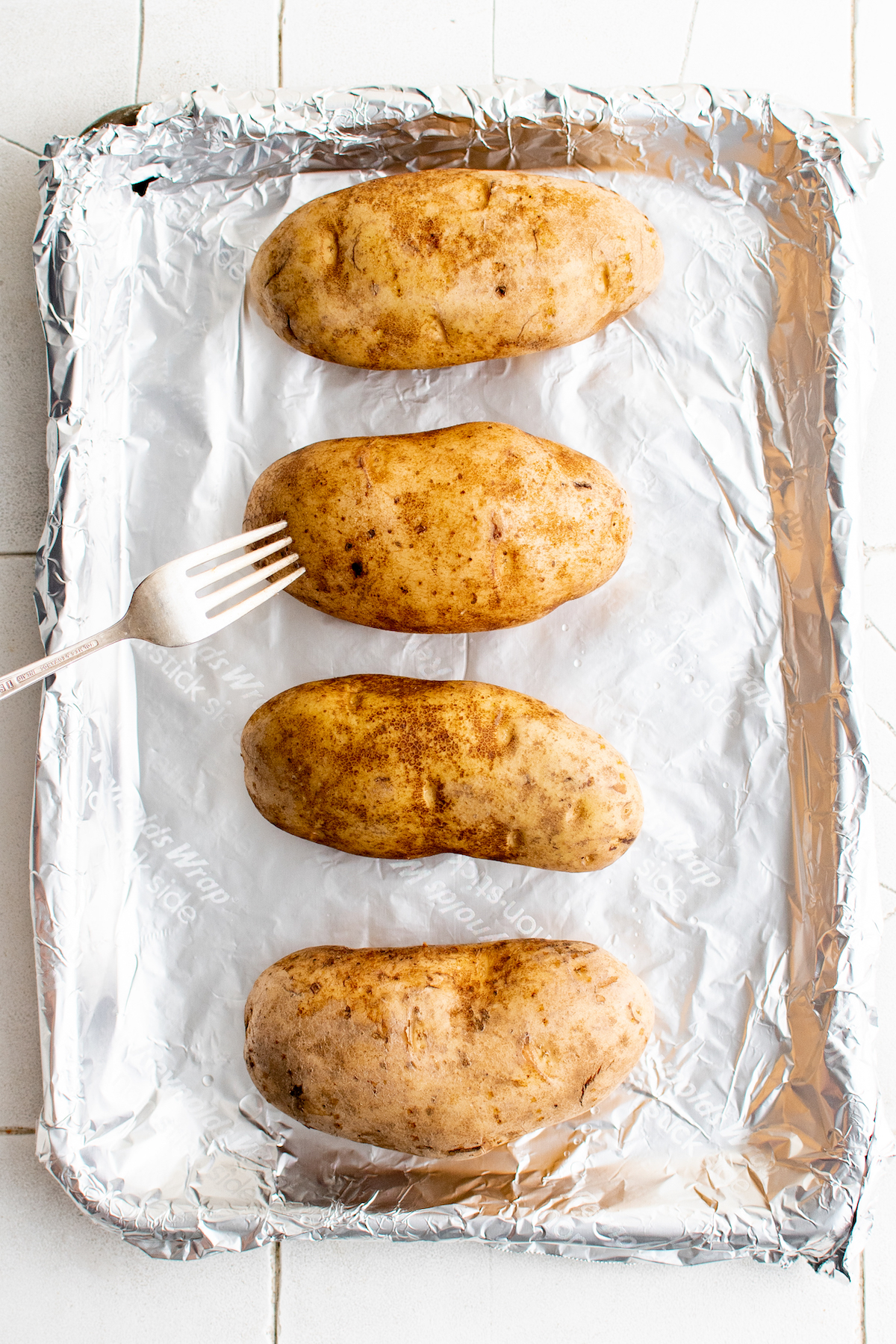 Four potatoes on a baking sheet with a fork.