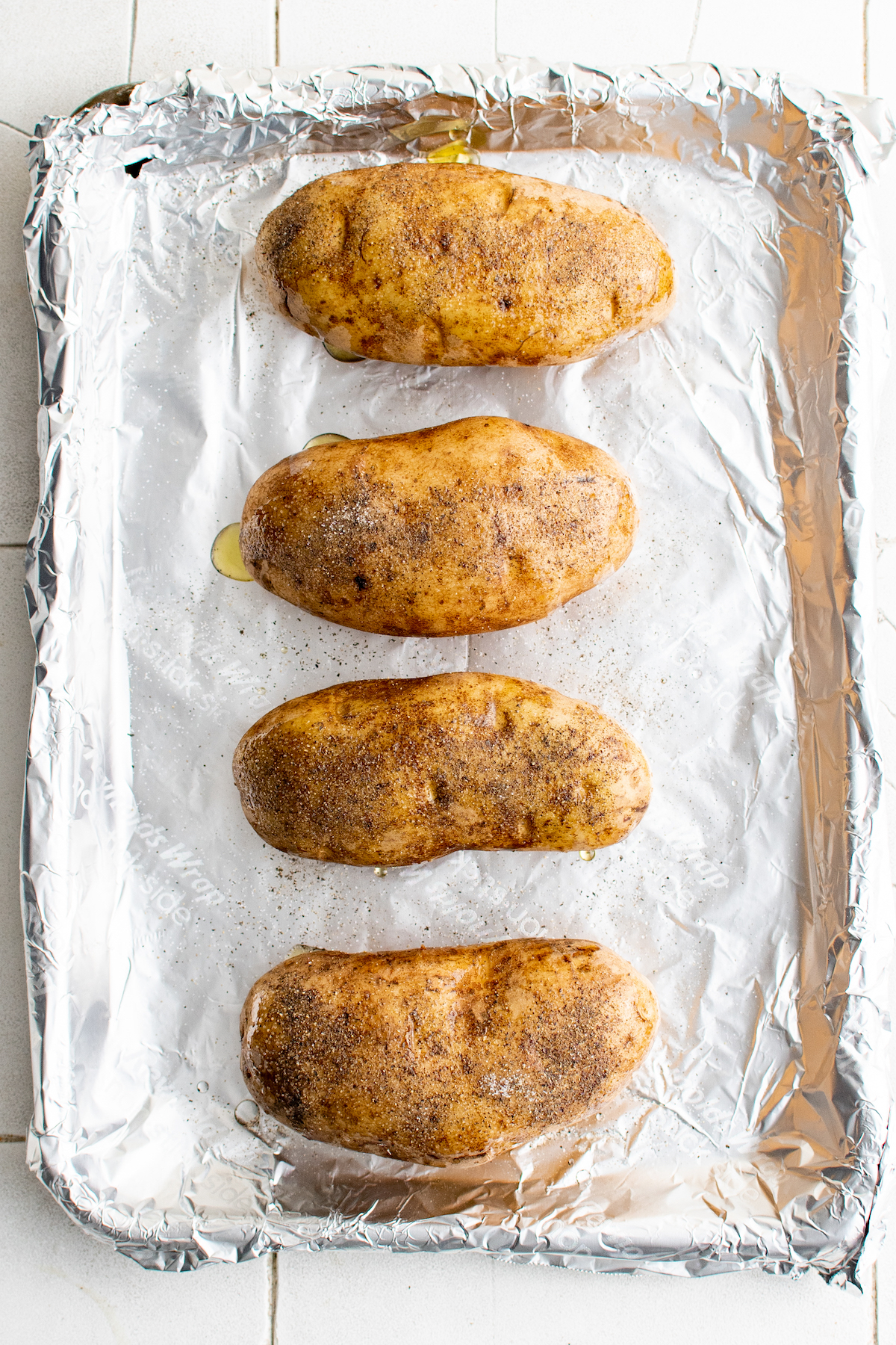 Four potatoes on a baking sheet, oiled and seasoned.