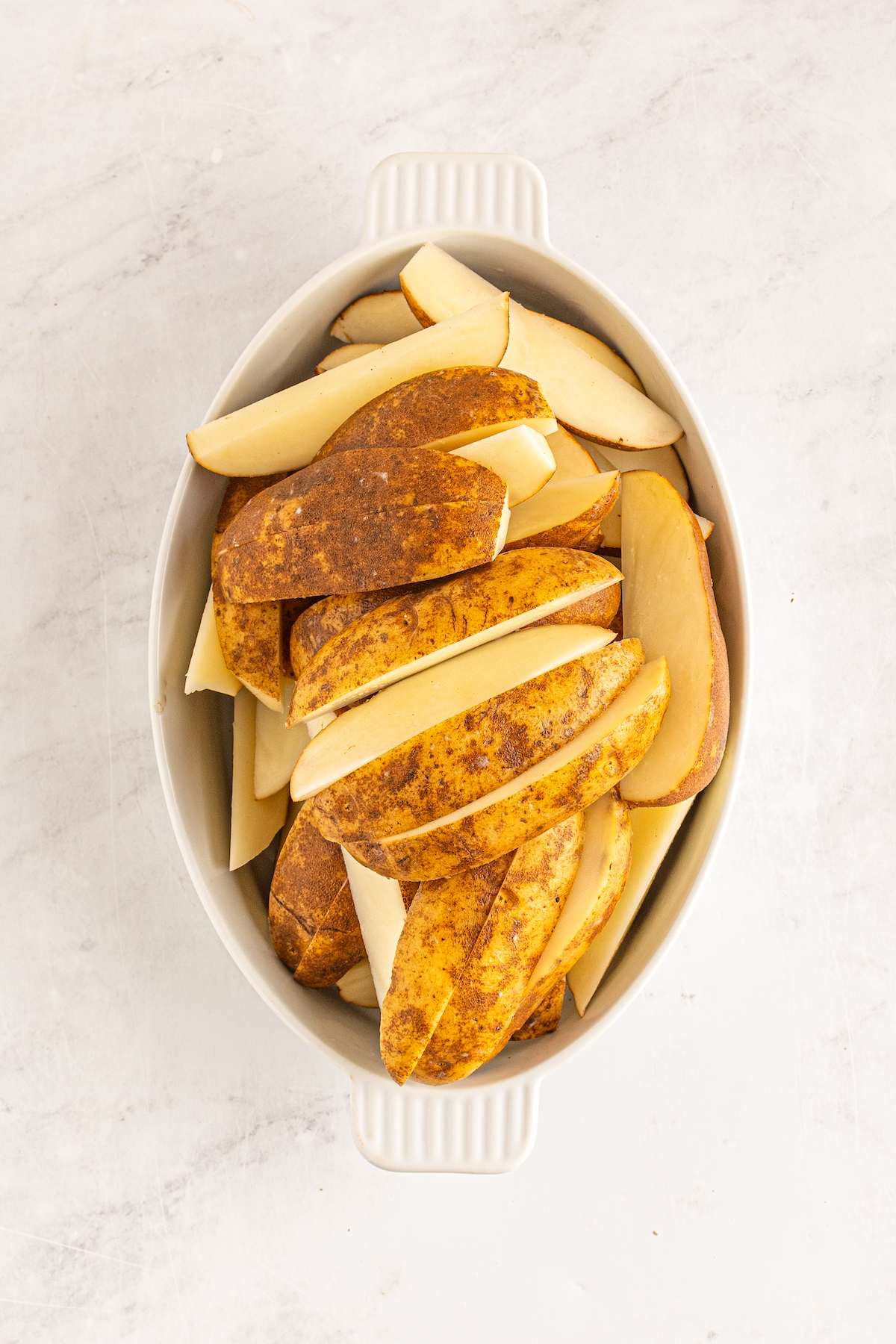 An oval-shaped dish of raw potato wedges.