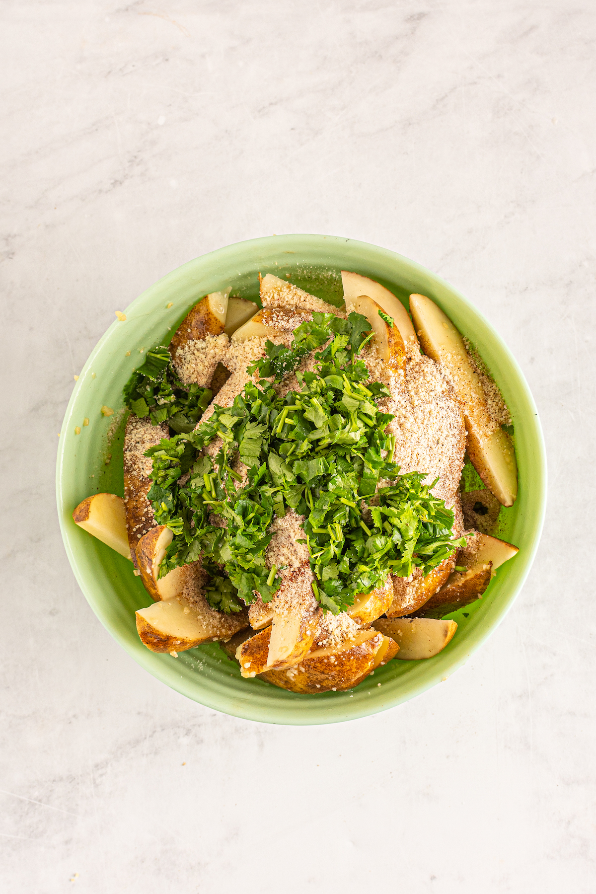 Seasoned, uncooked potatoes in a bowl with fresh herbs and parmesan.