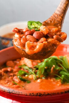 A pot of charro beans with a wooden spoon scooping out a serving of beans.
