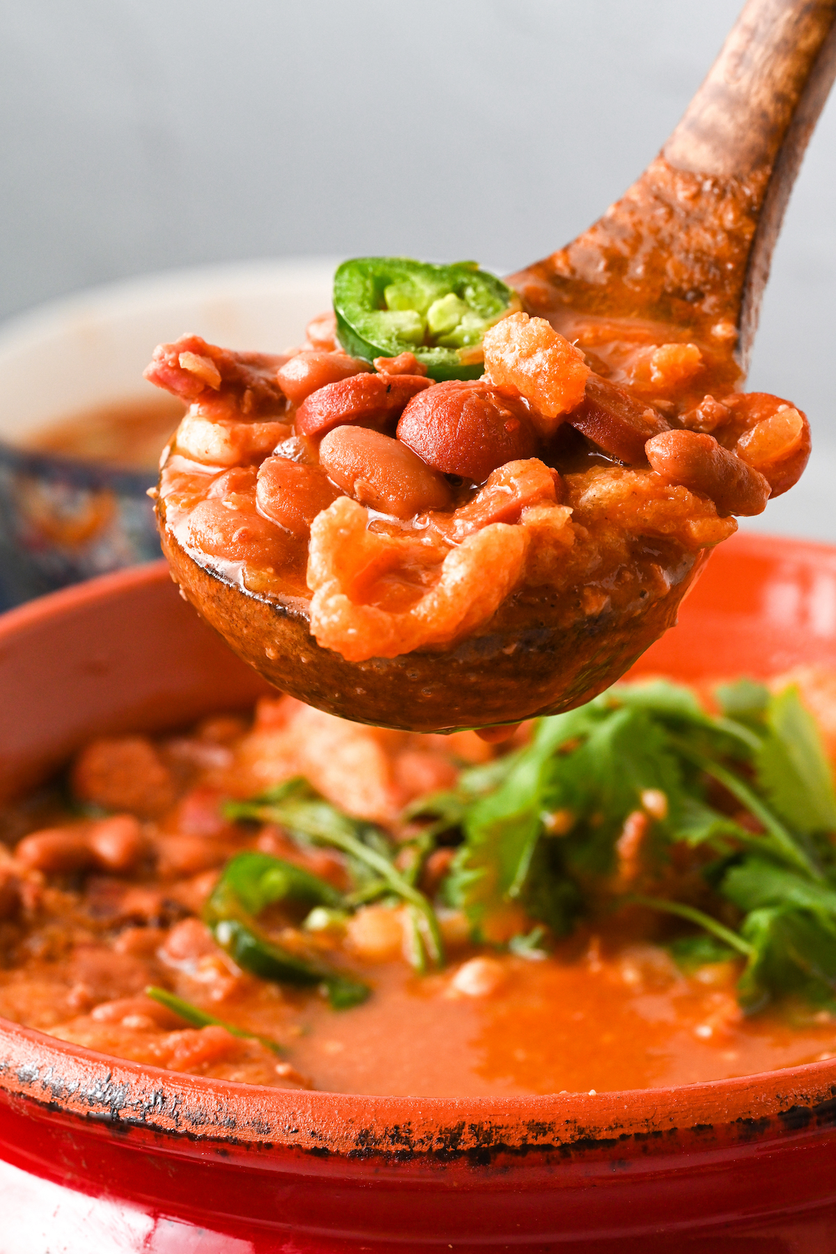 A pot of charro beans with a wooden spoon scooping out a serving of beans.