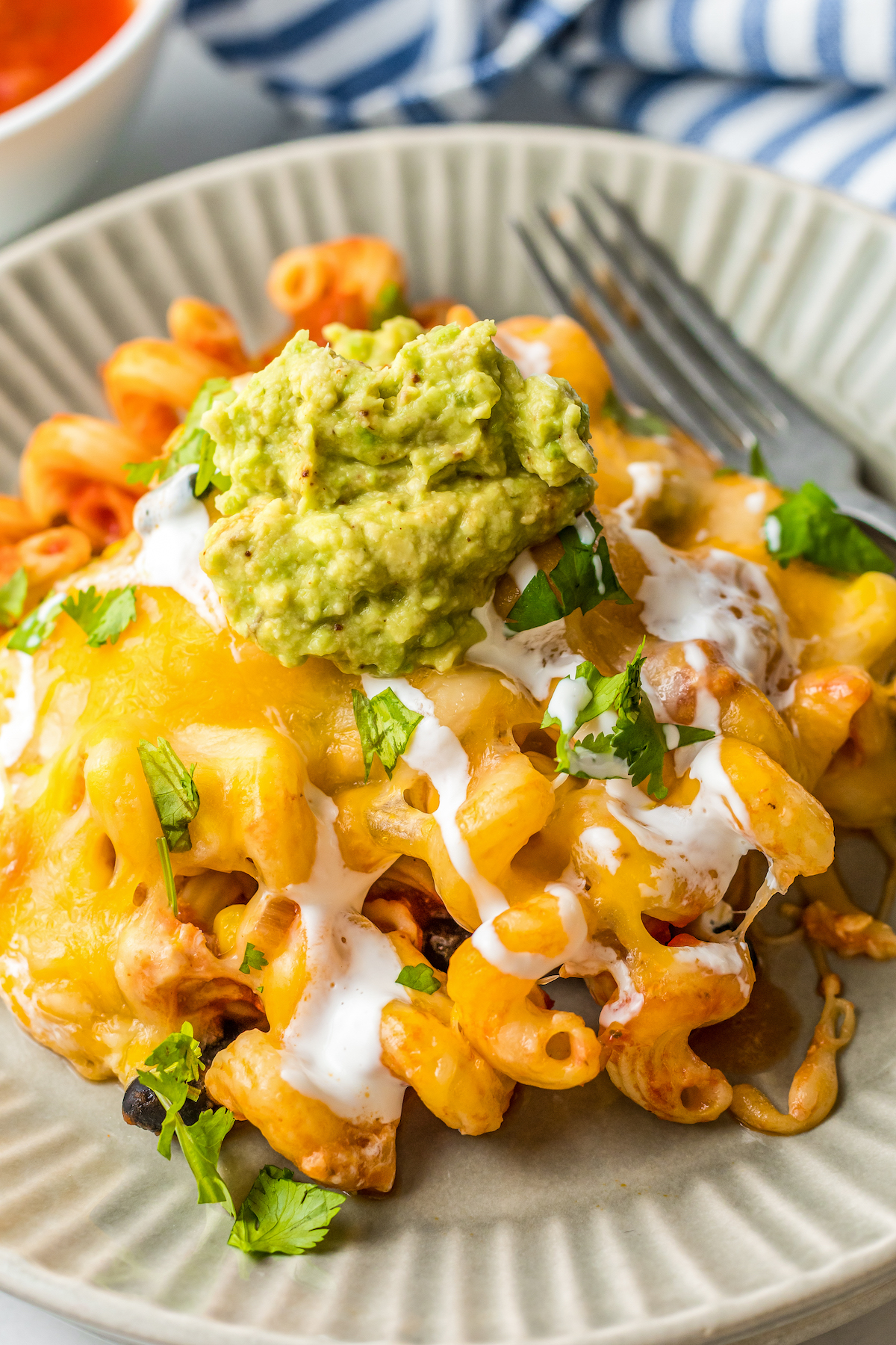 A plate of Chicken Enchilada Pasta Bake with sour cream, cilantro and guacamole on top.