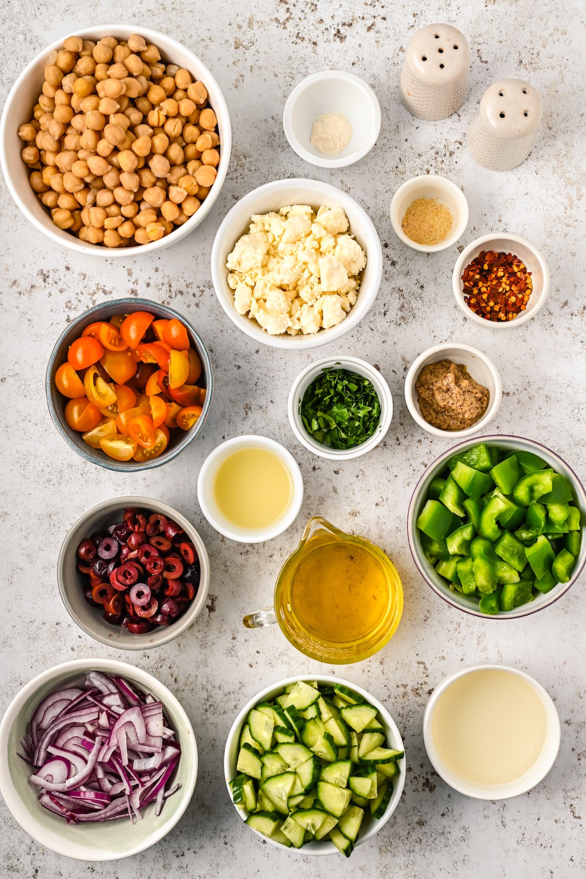Chickpeas, spices, feta, bell pepper, olives, and other ingredients for chickpea salad measured into small dishes and arranged on a work surface.