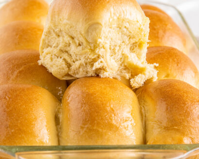 A pan of dinner rolls, with one removed from the pan and placed on top of the others.