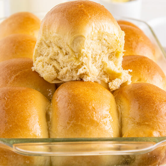 A pan of dinner rolls, with one removed from the pan and placed on top of the others.