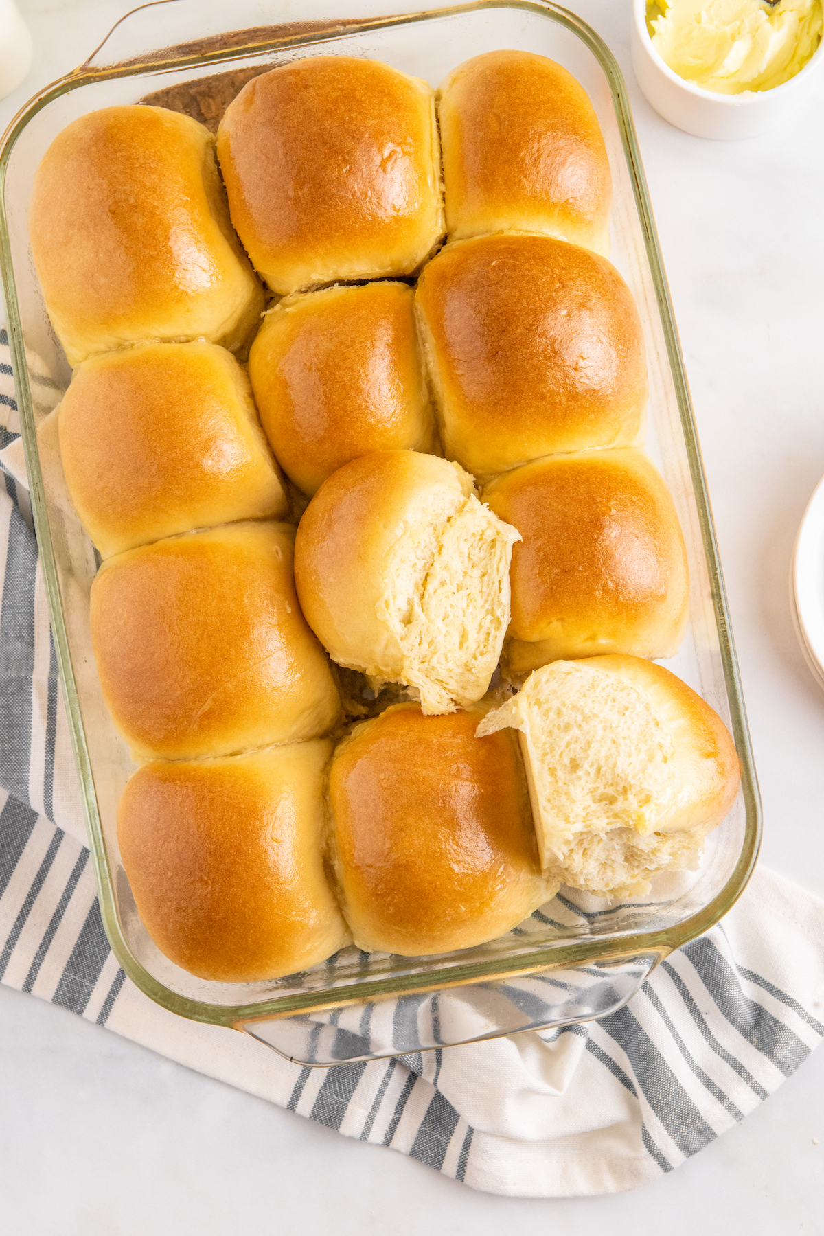 A pan of rolls, with one roll torn in half and placed on top of the others.
