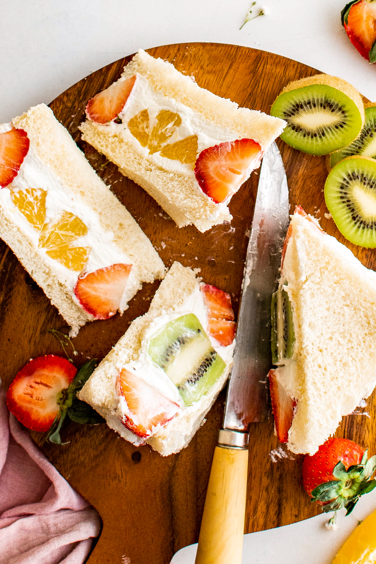A wooden cutting board with fruit and a whipped cream sandwich.