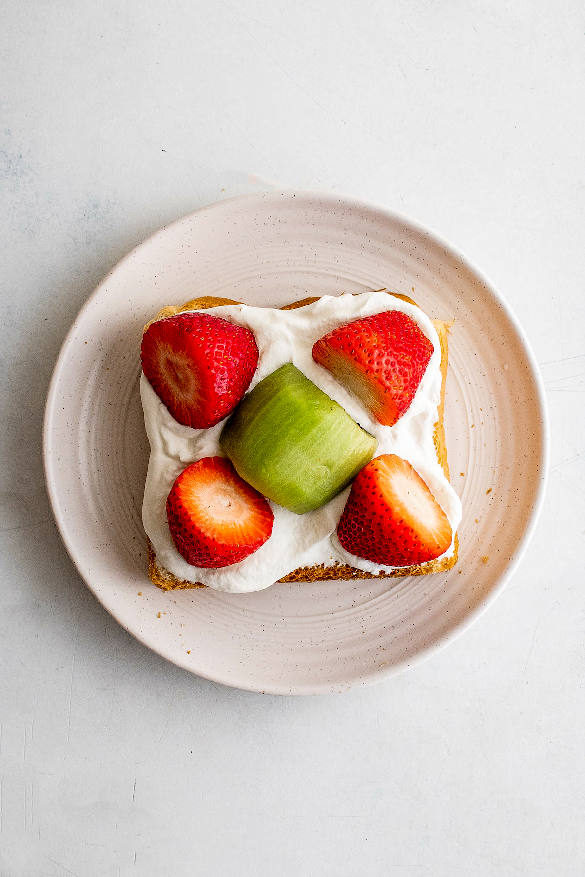 A slice of bread covered in whipped cream, with fruit arranged symmetrically on top.