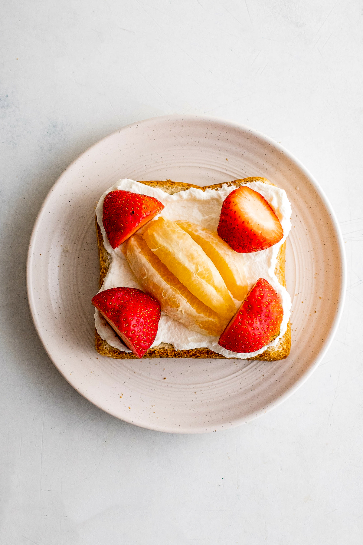 A piece of sandwich bread topped with whipped cream, strawberries, and orange segments.
